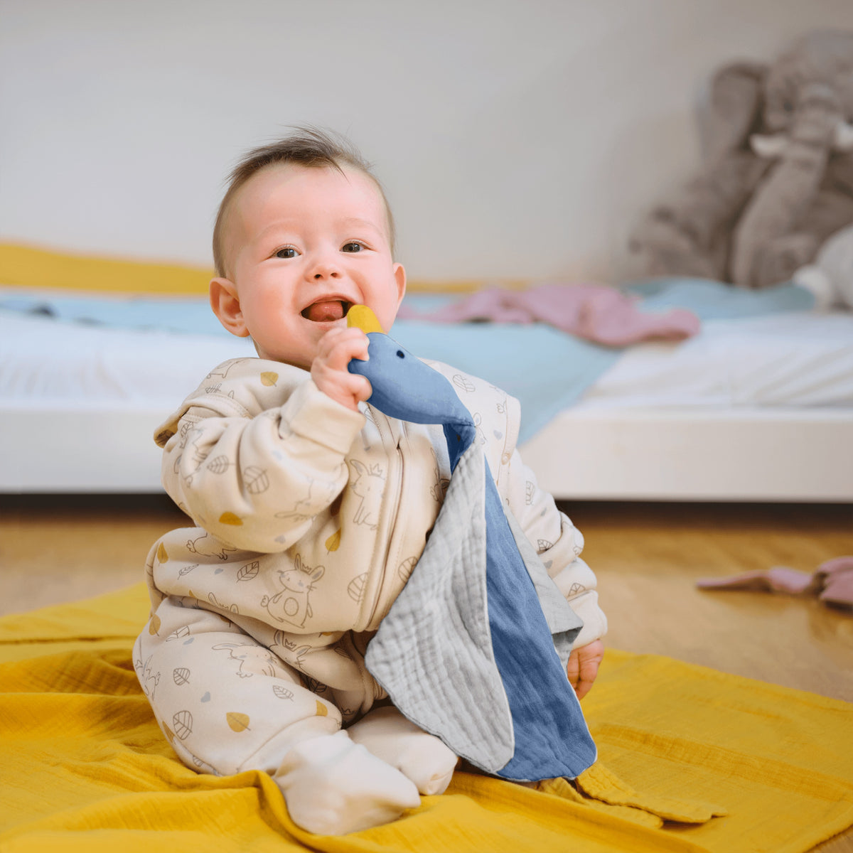 Baby im Schlafsack mit Füßen auf einer Musselindecke hält die Schmuse-Ente